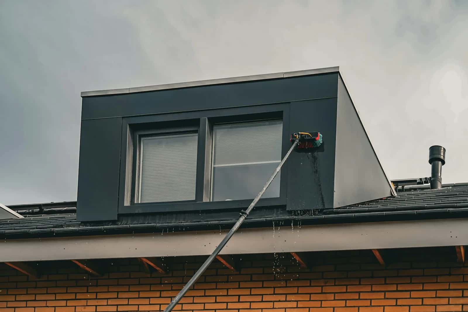Technician cleaning weathered fascias and soffits with telescopic pole