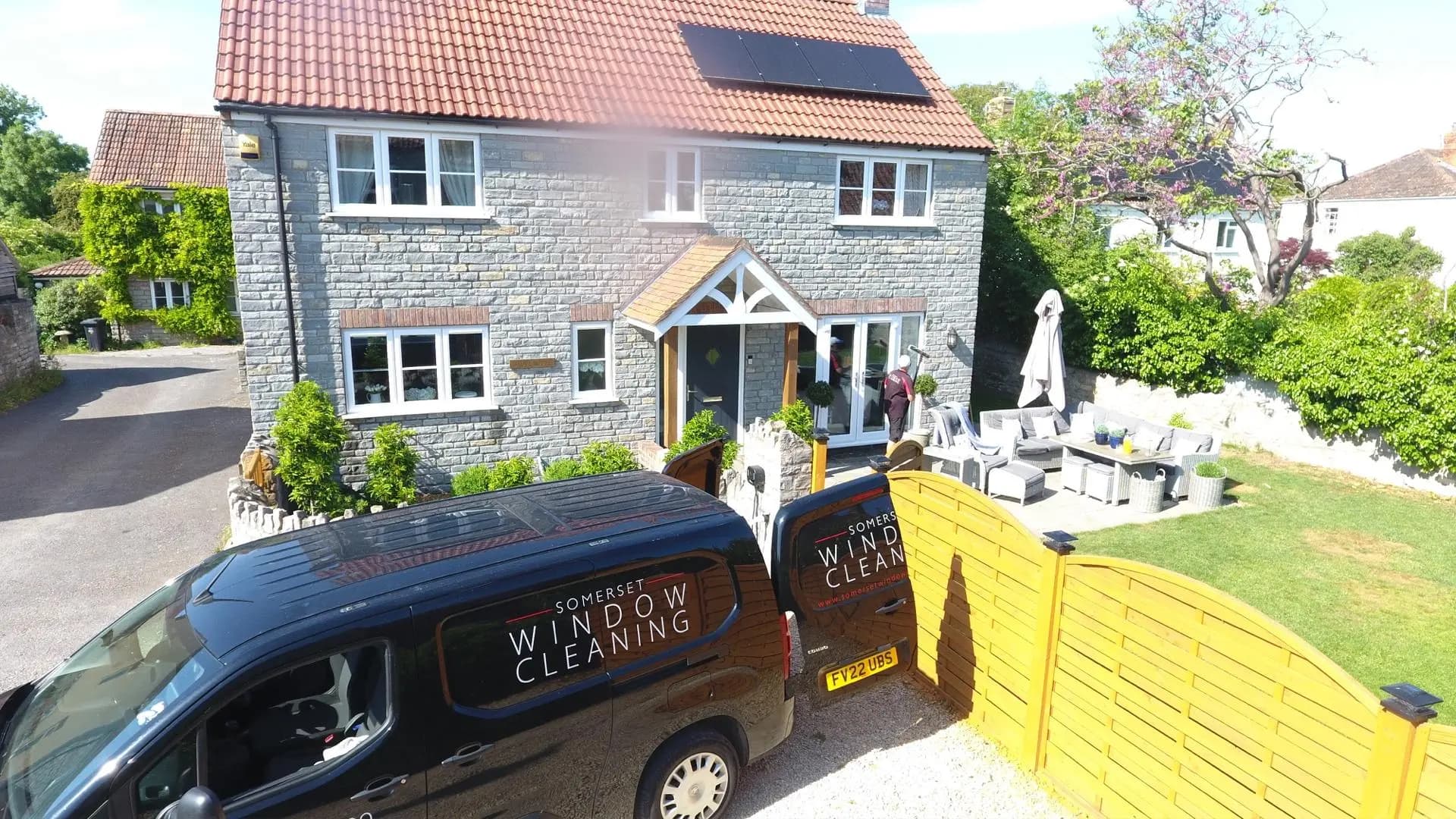 Somerset Window Cleaning van parked outside a stone village home with a technician at the front door