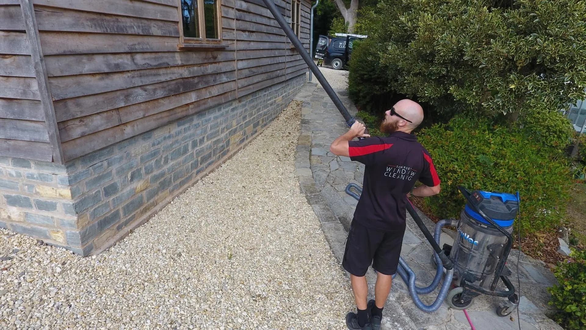 Somerset Window Cleaning technician clearing gutters on a timber-clad building with a gutter vacuum pole