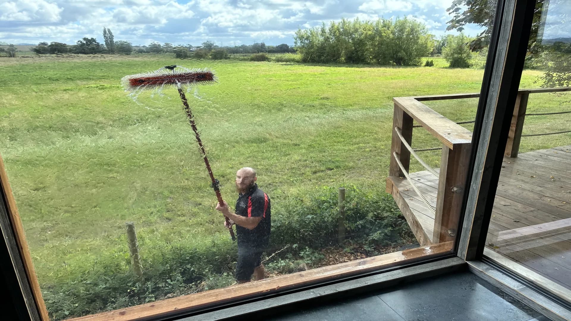 Reach-and-wash brush head rinsing a large picture window with pure water, seen from inside