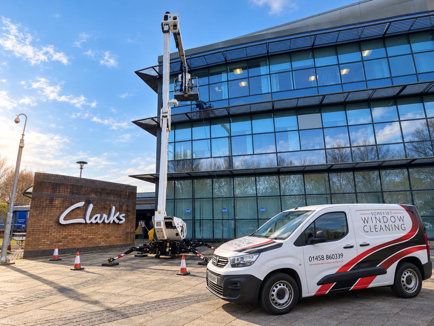 Edited photo of a cherry picker at the Clarks building in Street, with the Clarks sign visible, a white Somerset Window Cleaning van added and brighter daylight