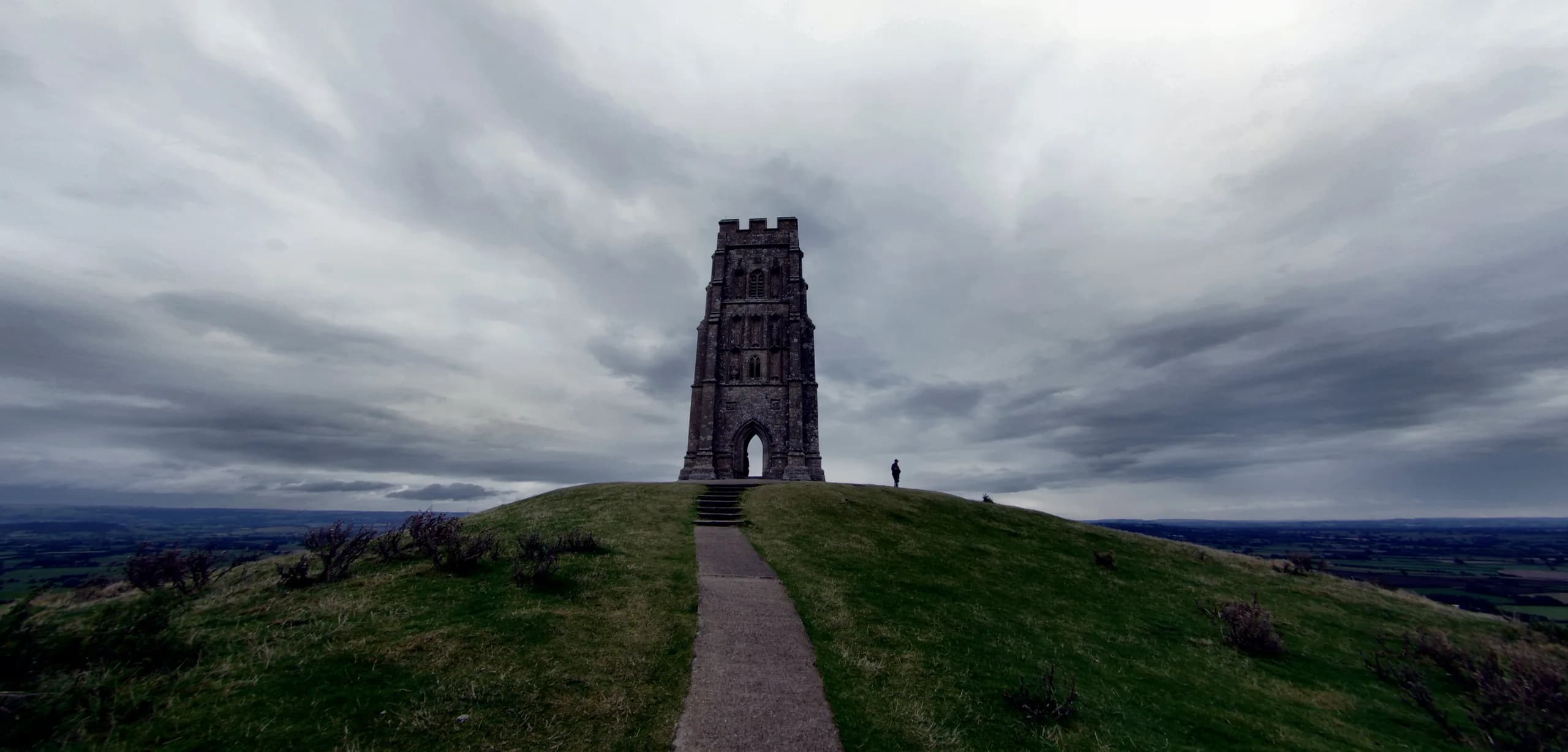 Glastonbury Tor under a brooding sky, with the Somerset Levels beyond