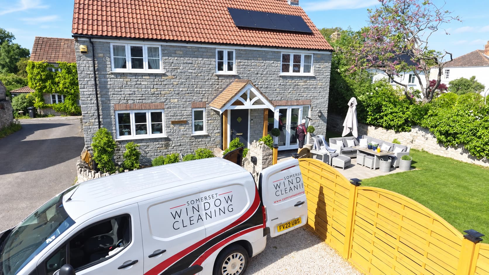 Edited photo of a Somerset village home with a technician at the front door; white Somerset Window Cleaning van added and lawn colour retouched