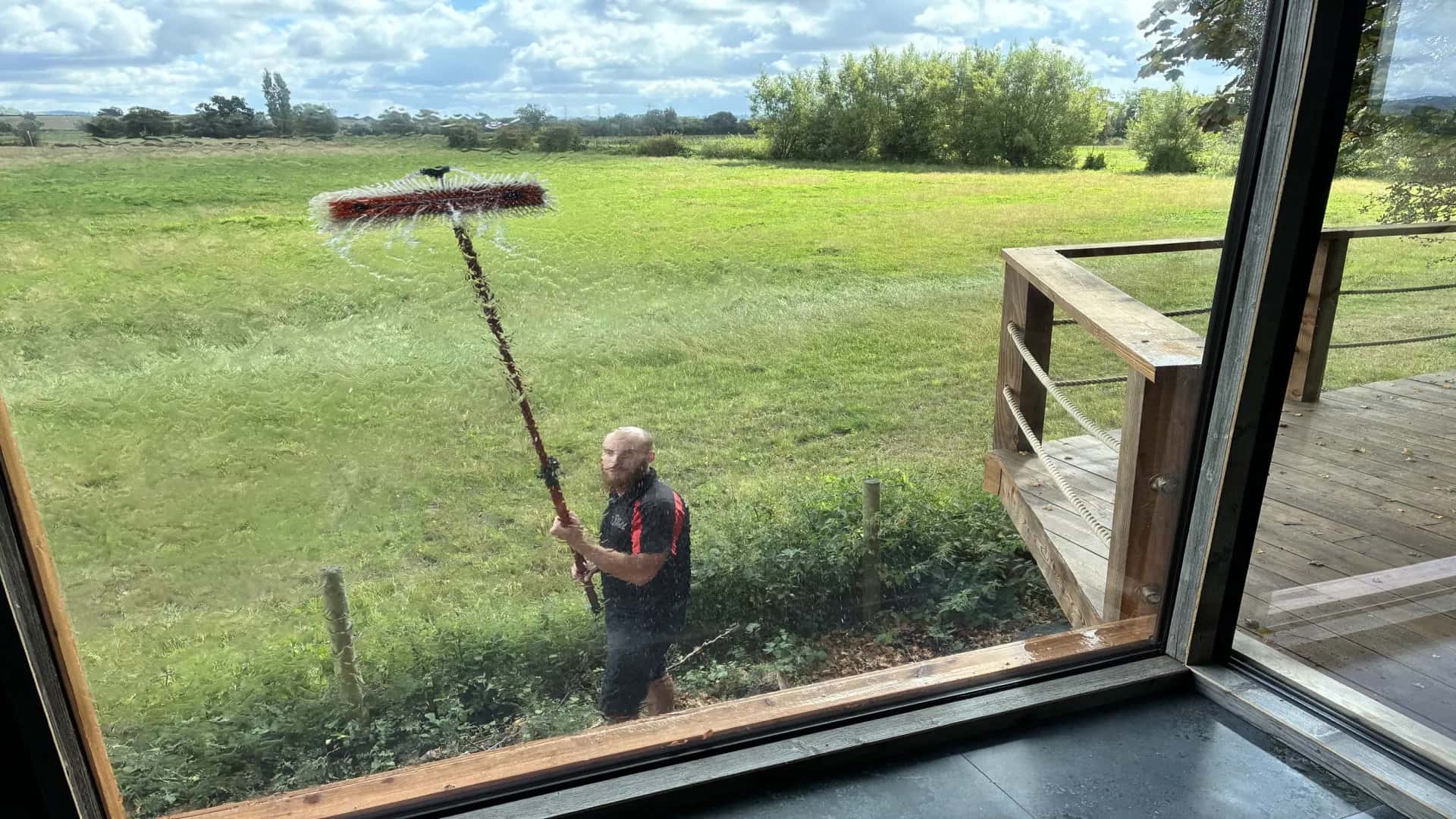 A Somerset Window Cleaning cleaner using a reach-and-wash pole outside a rural home