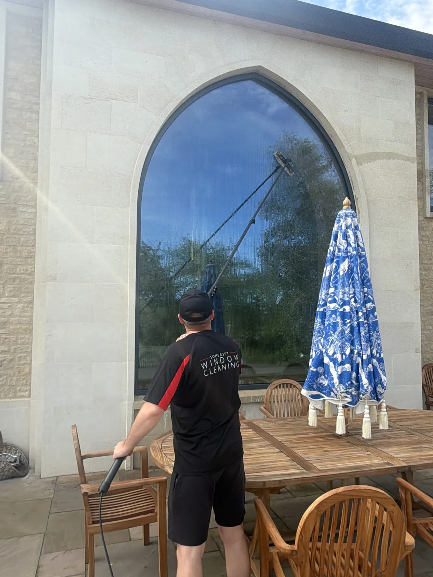 A Somerset Window Cleaning technician cleaning a large arched window with a reach-and-wash pole brush