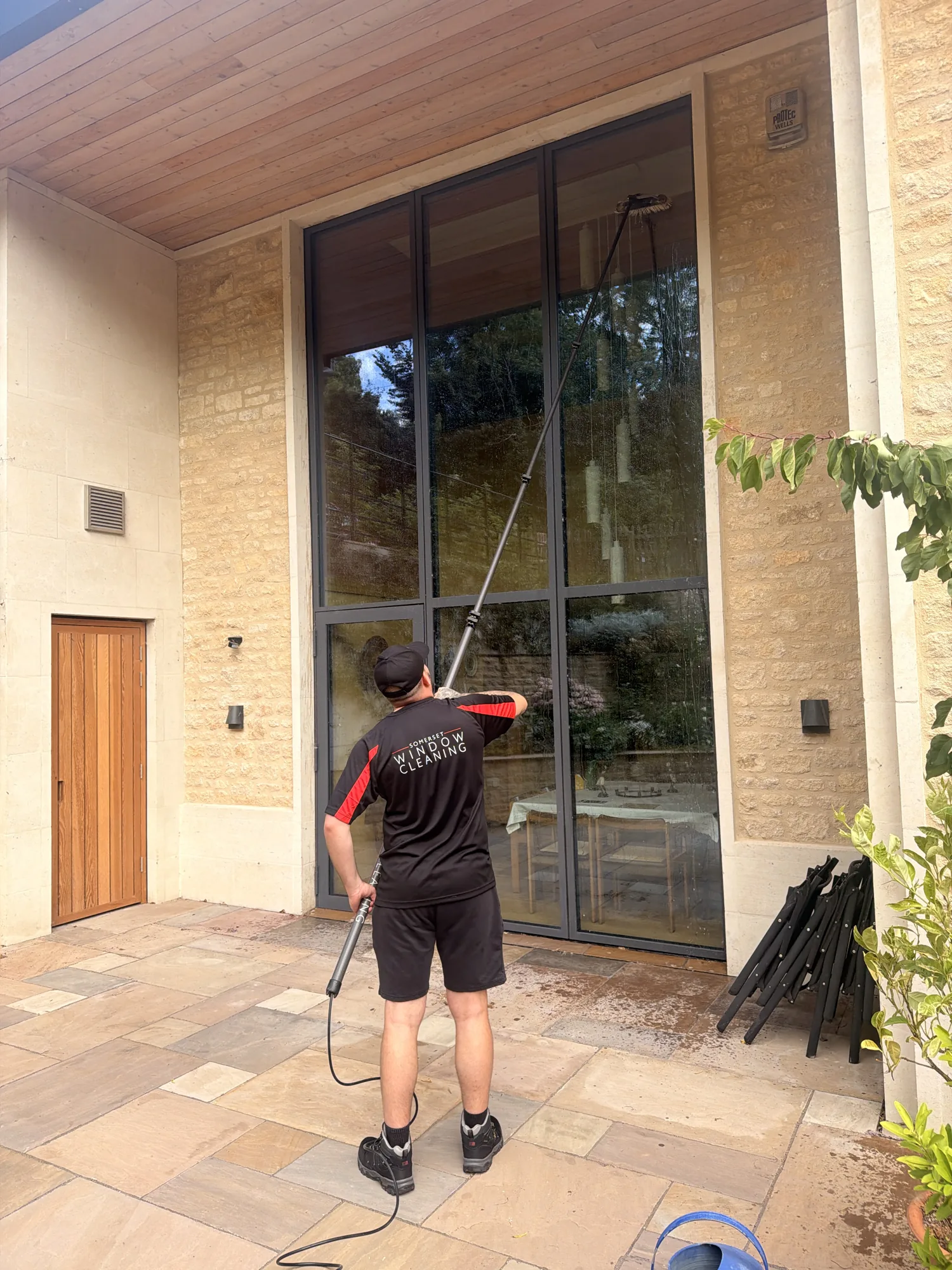 A Somerset Window Cleaning technician cleaning tall glazing with a reach-and-wash pole at a Somerset home