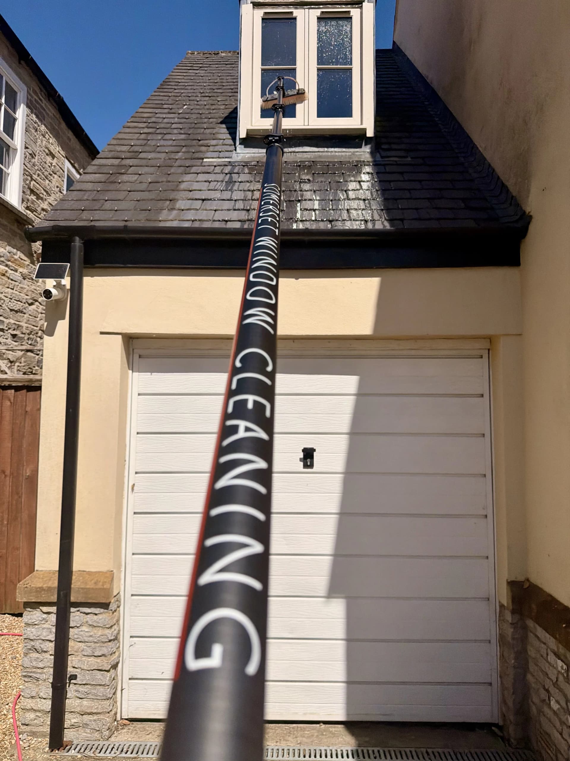 A Somerset Window Cleaning reach and wash pole cleaning an upstairs window from the ground